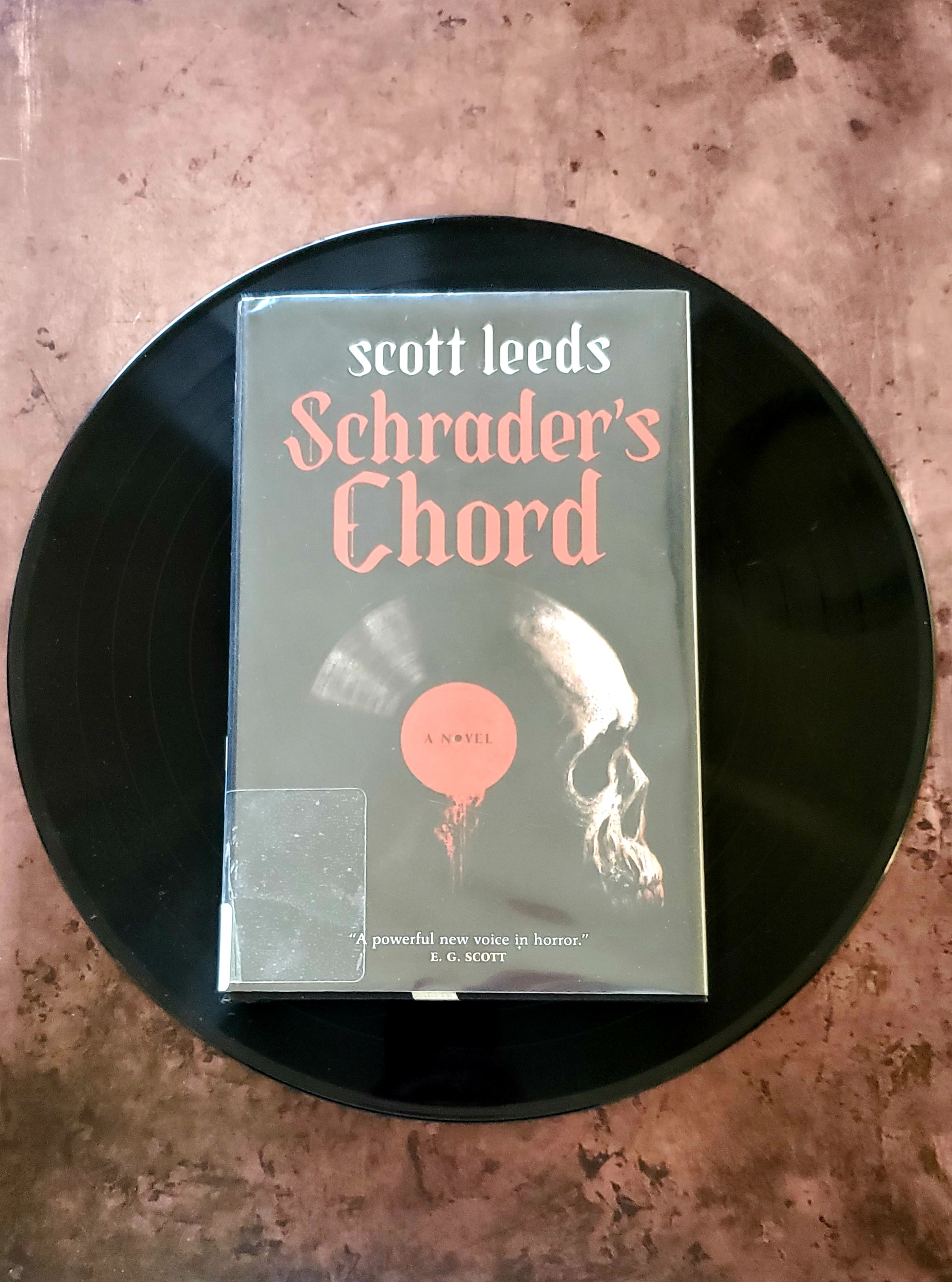 Book cover of Schrader's Chord by Scott Leeds, resting on a music vinyl record